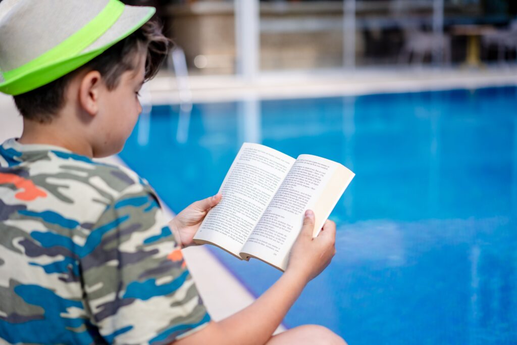 A boy read a book at the swimming pool