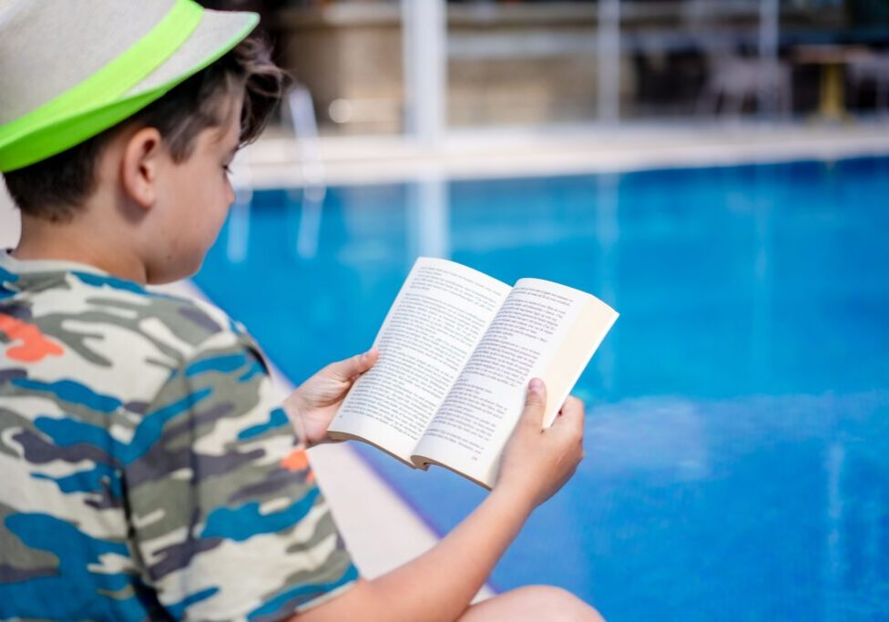 A boy read a book at the swimming pool